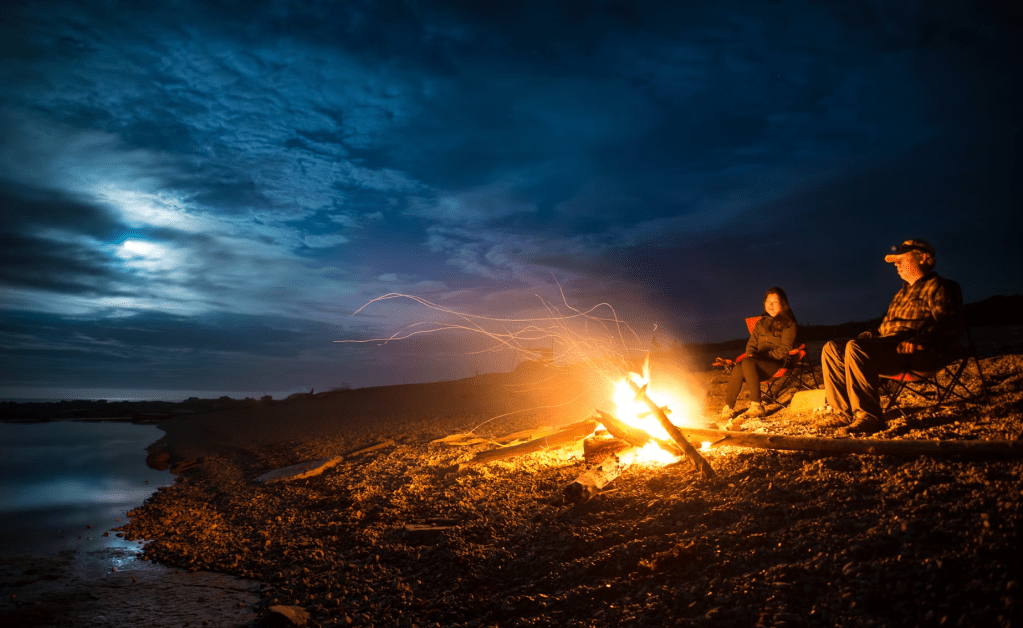 Night time campfire on a rocky beach of Prince Edward Islands underneath a cloudy moonlit sky.